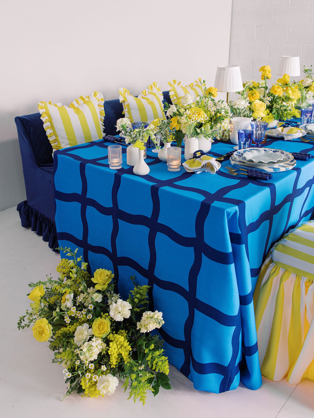 Blue tablecloth with white vases and plates with yellow flower arrangements