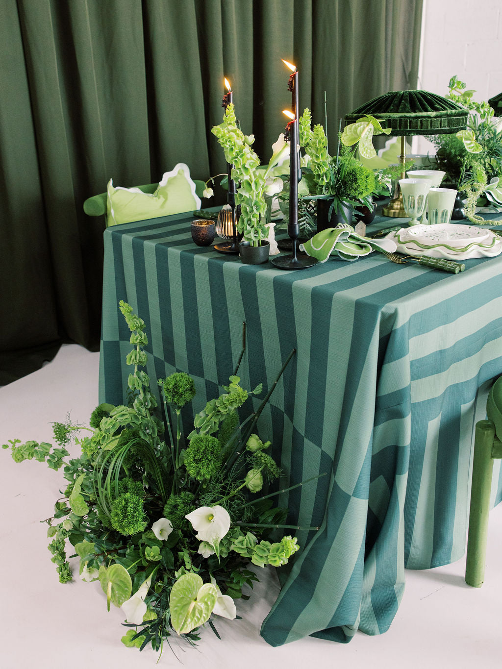 Decorative table setting with green and white striped tablecloth, candles, and floral arrangements.