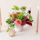 Floral arrangement with candles and small lights on a white surface