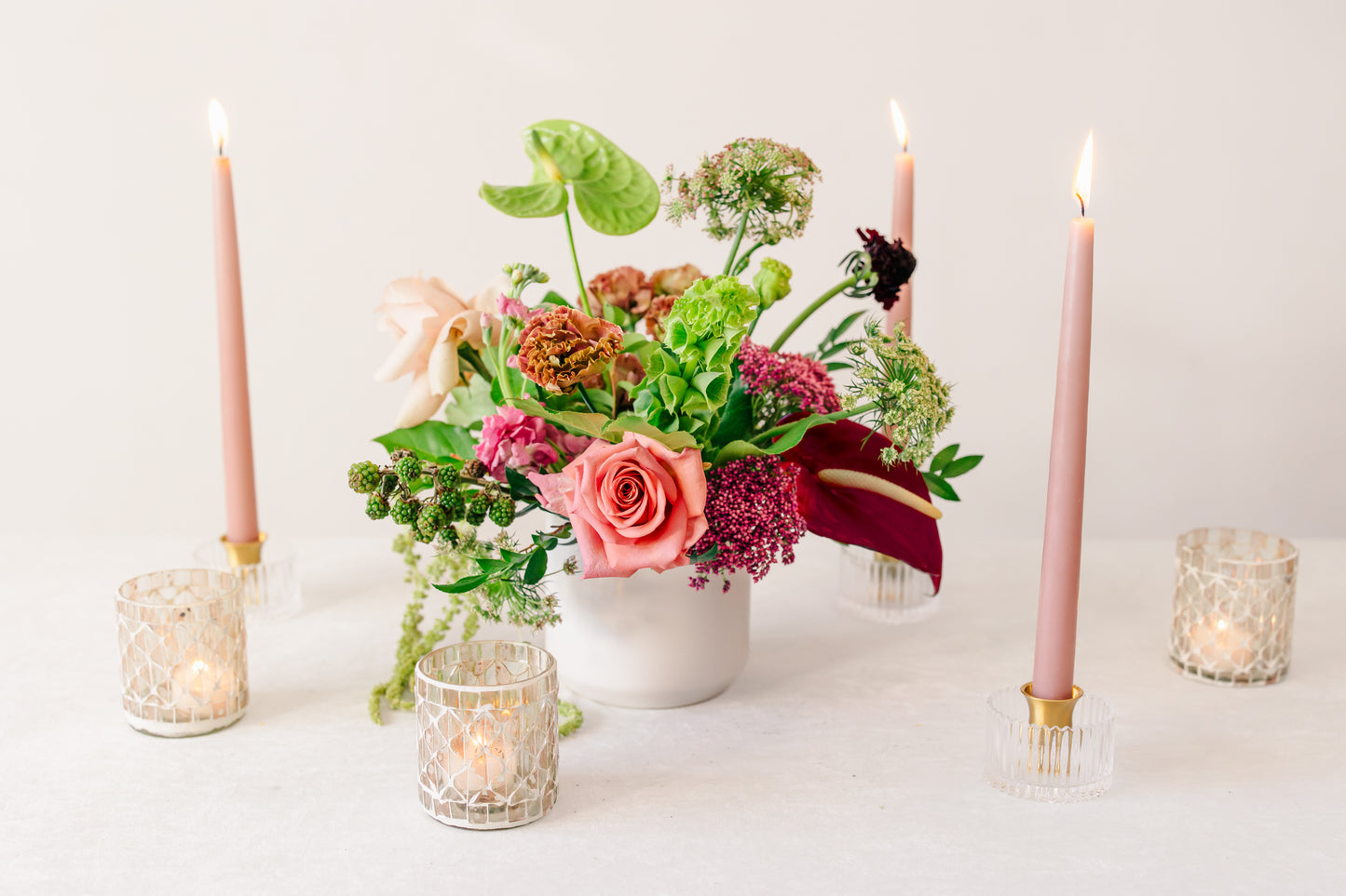 Floral arrangement with candles and small lights on a white surface