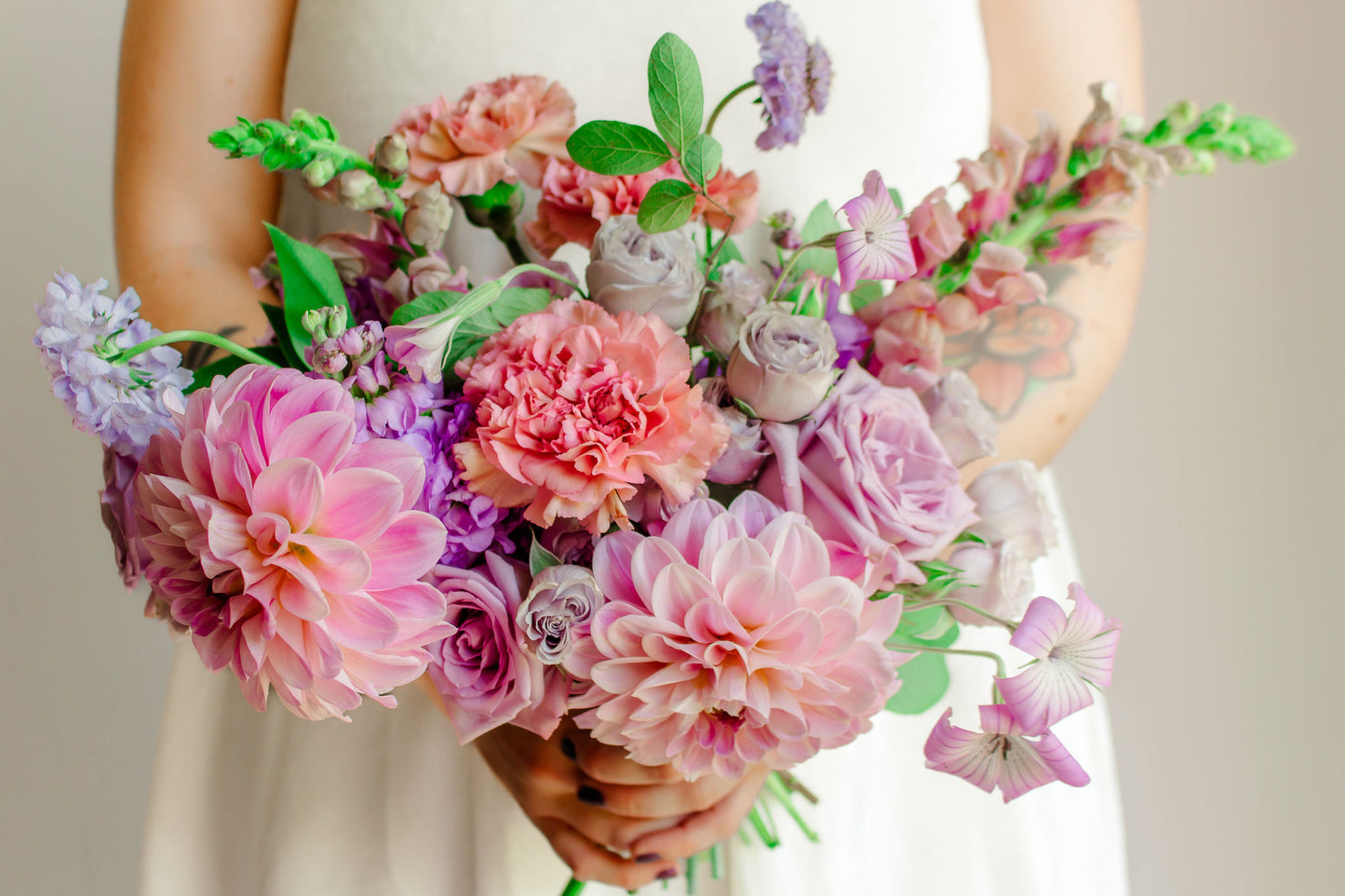 Garden style bridal bouquet of light purple and light pink flowers, such as dahlias, roses, snapdragons, carnations, stock, scabiosa, and corncockle.