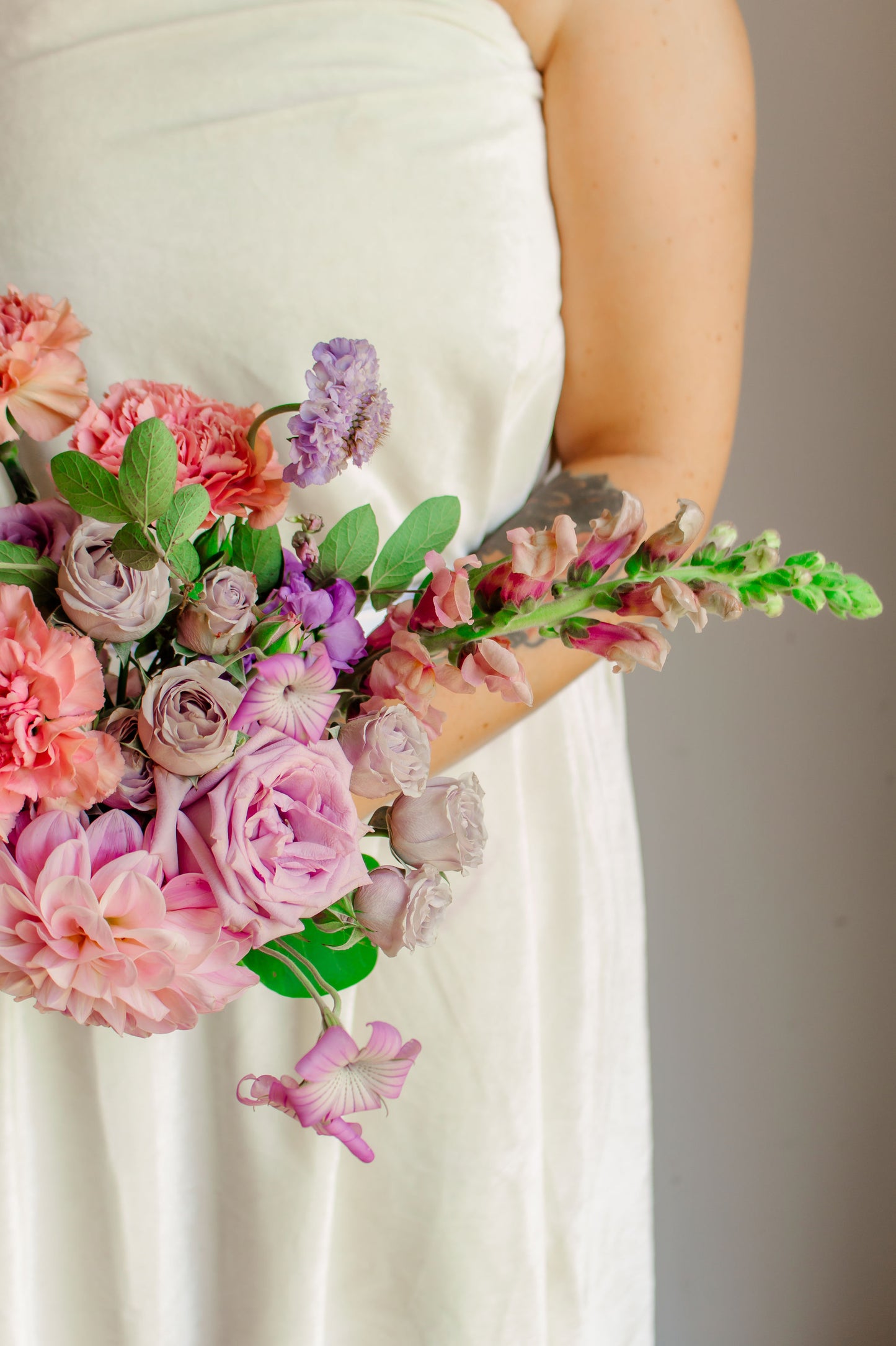 Garden style bridal bouquet of light purple and light pink flowers, such as dahlias, roses, snapdragons, carnations, stock, scabiosa, and corncockle.