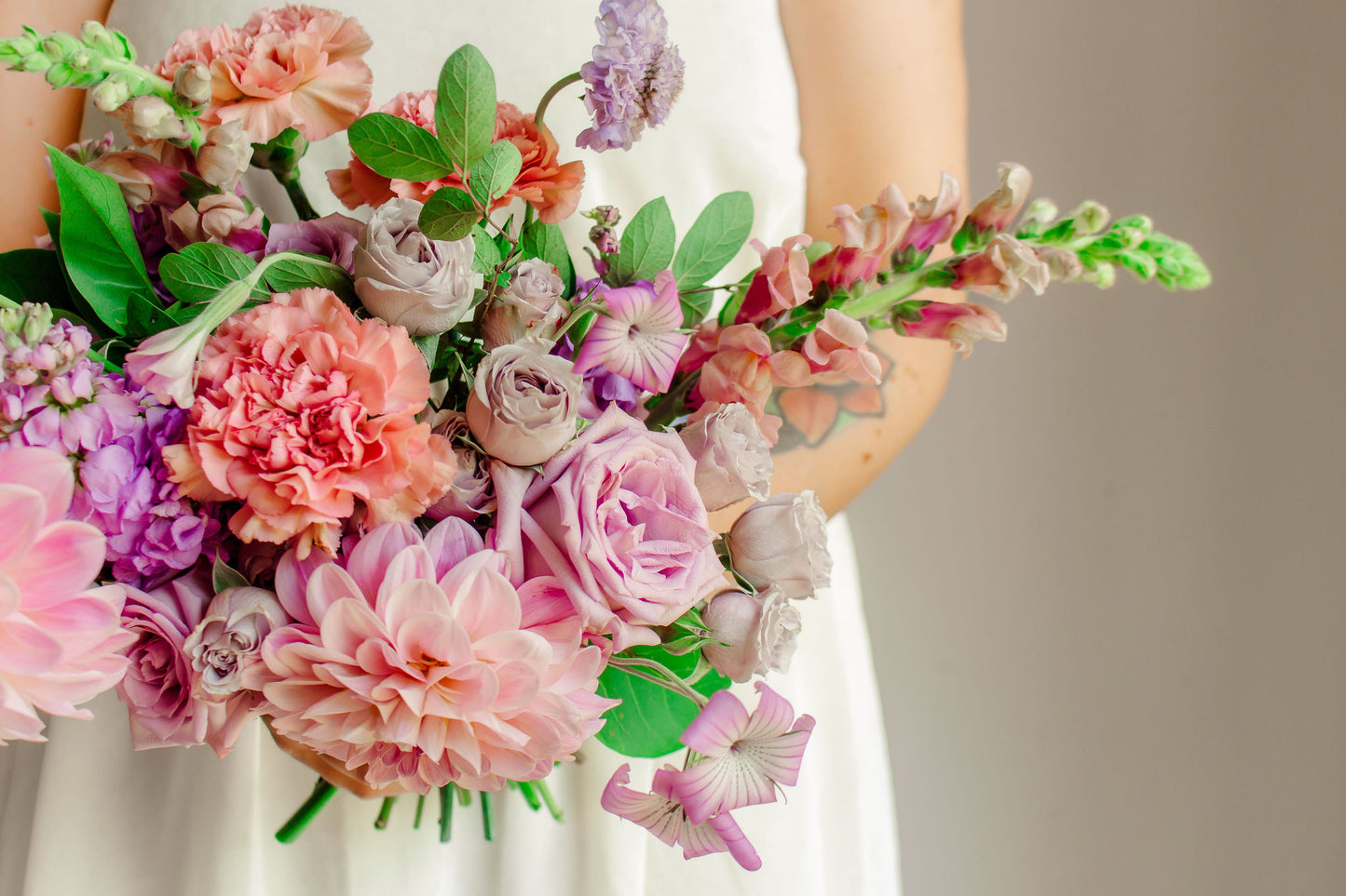 Garden style bridal bouquet of light purple and light pink flowers, such as dahlias, roses, snapdragons, carnations, stock, scabiosa, and corncockle.