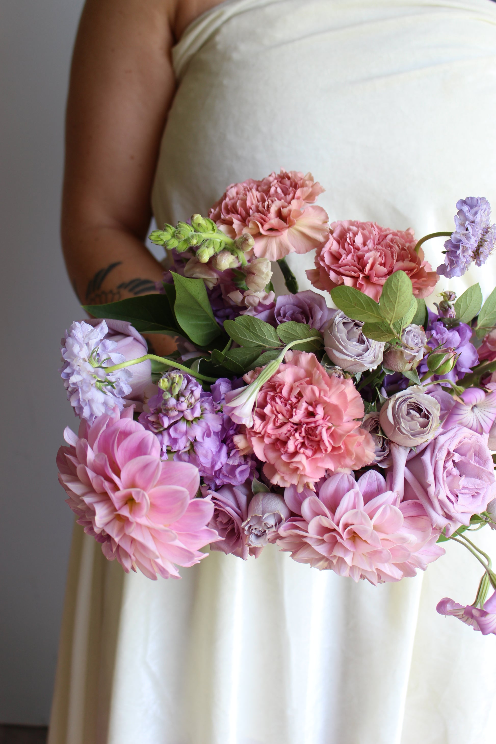 Garden style bridal bouquet of light purple and light pink flowers, such as dahlias, roses, snapdragons, carnations, stock, scabiosa, and corncockle.