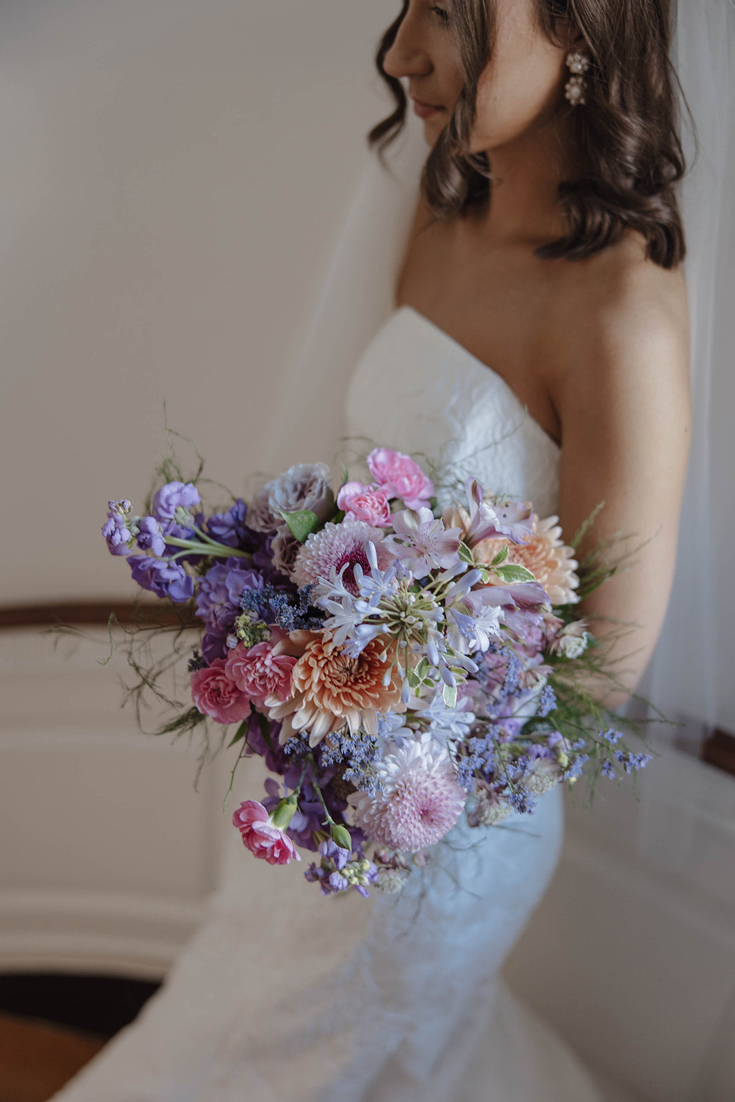 Bride holding a garden style bridal bouquet of light purple and light pink flowers, such as agapanthus, stock, carnations, mums, and spray roses.