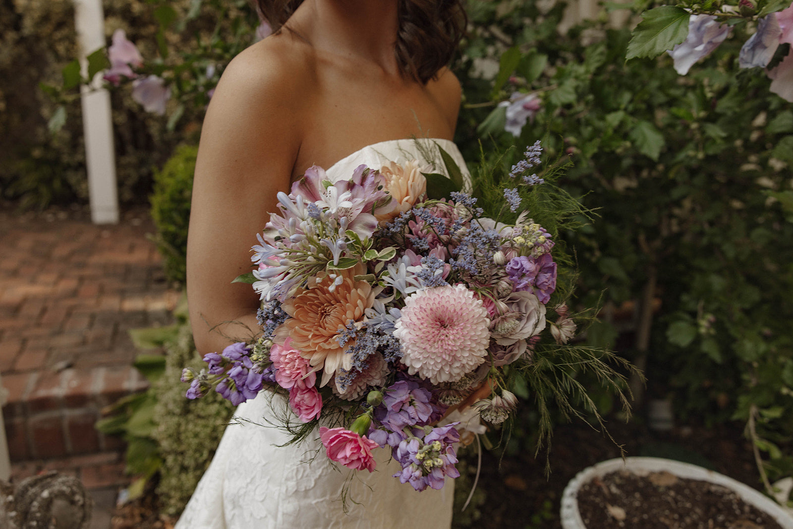 Bride holding a garden style bridal bouquet of light purple and light pink flowers, such as agapanthus, stock, carnations, mums, and spray roses.