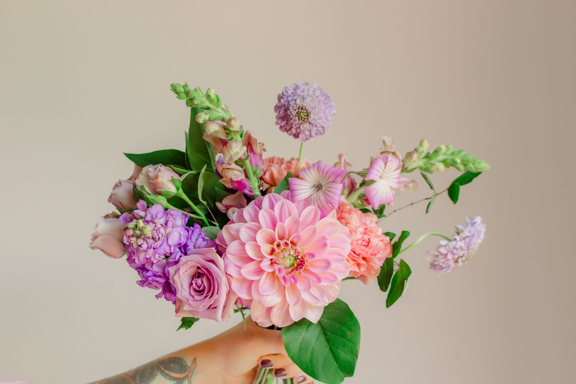 A small bouquet of lavender, mauve, and purple flowers, such as dahlias, sotck, carnations, snapdragons, and corncockle.