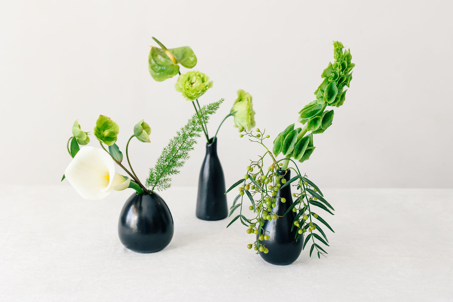 Three black vases with greenery on a white background