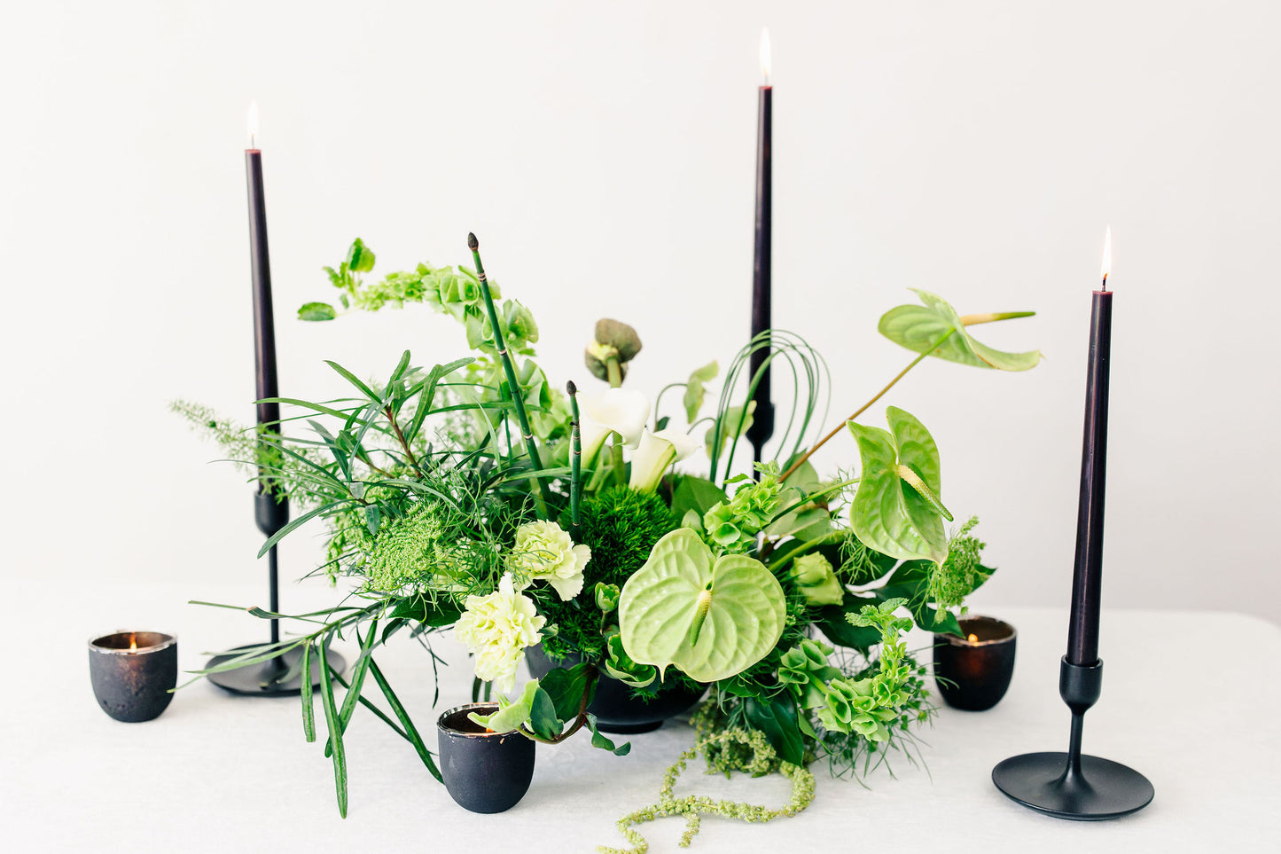 Green floral arrangement with black candles on a white background