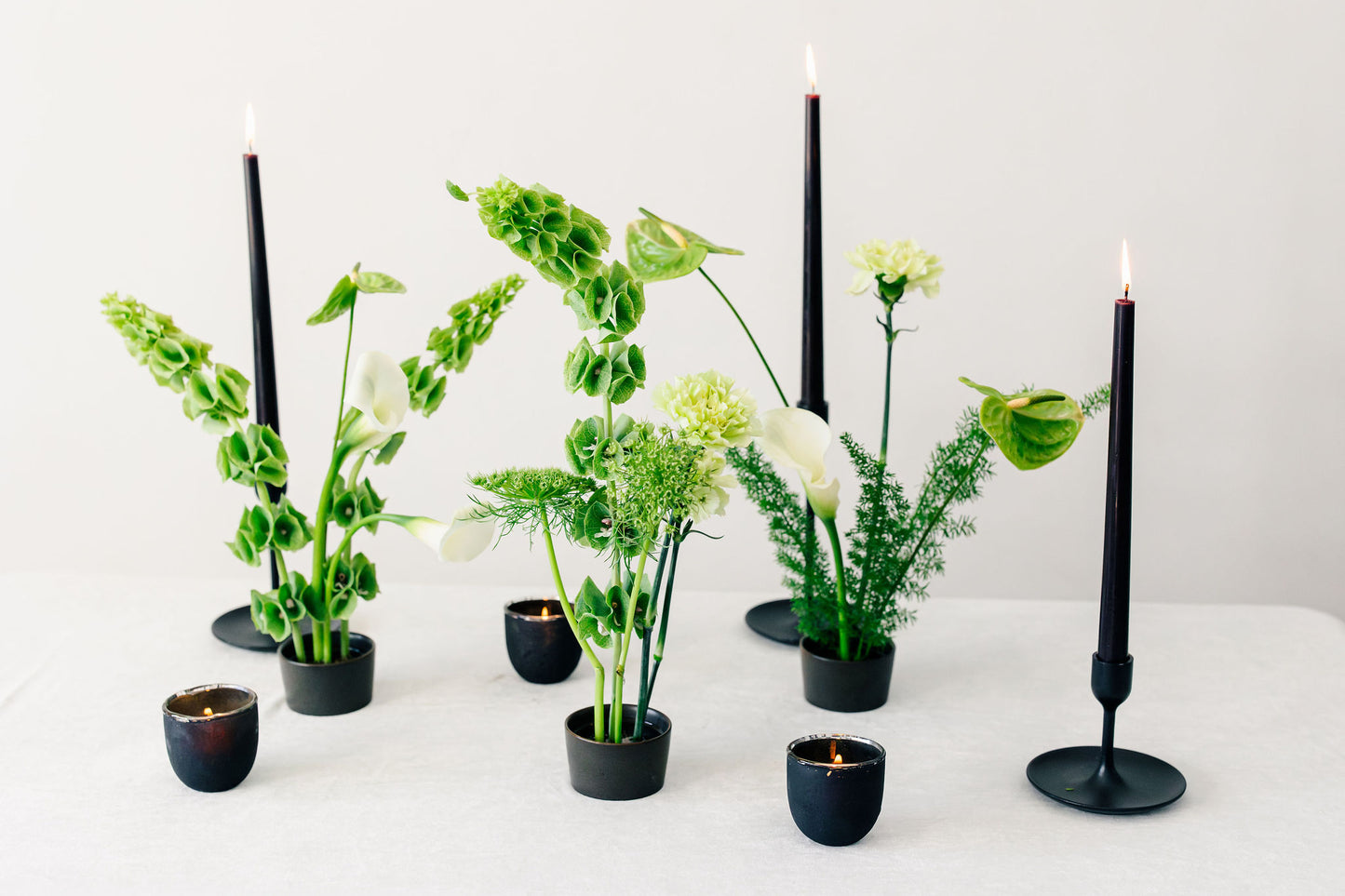 Decorative setup with black candles and green ikebana arrangements on a white surface