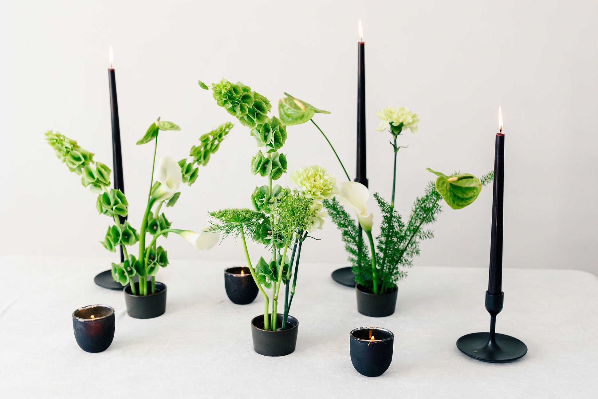 Decorative setup with black candles and green ikebana arrangements on a white surface