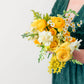 Person holding a bouquet of yellow and white flowers against a plain background