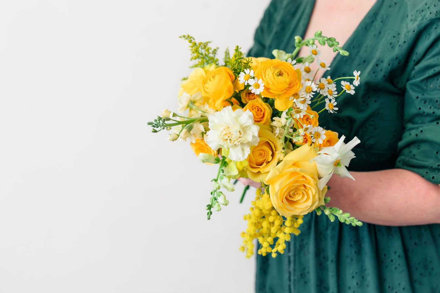 Person holding a bouquet of yellow and white flowers against a plain background