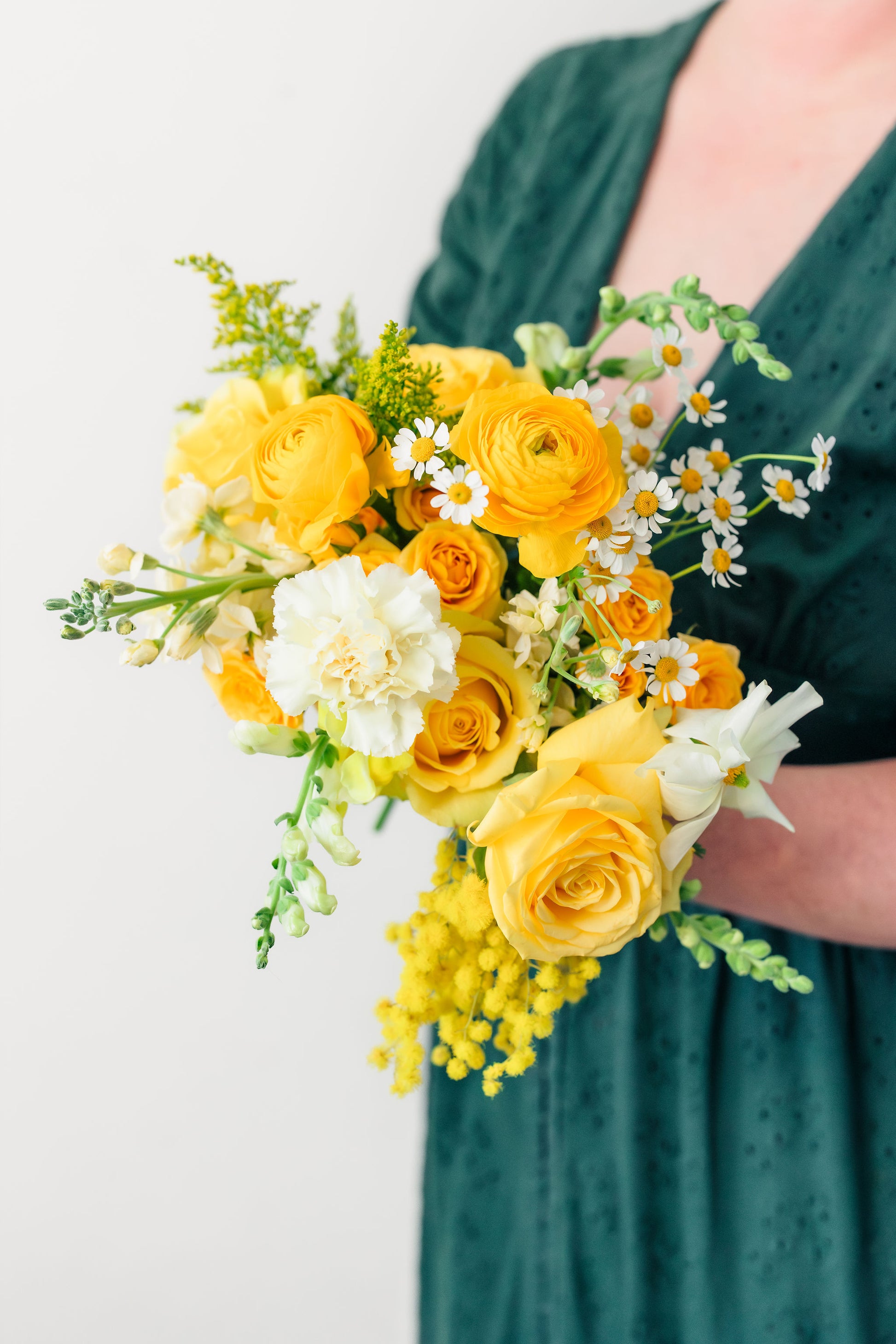 Bouquet of yellow and white flowers held by a person wearing a green dress.
