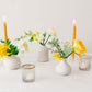 Yellow flowers in white bud vases with yellow candles on a white background