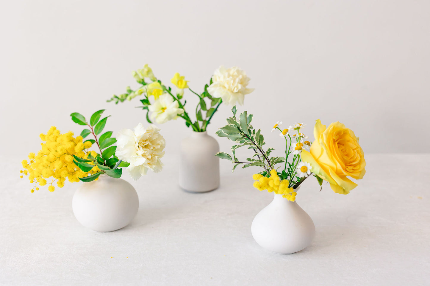 Yellow flowers in white bud vases on a white background