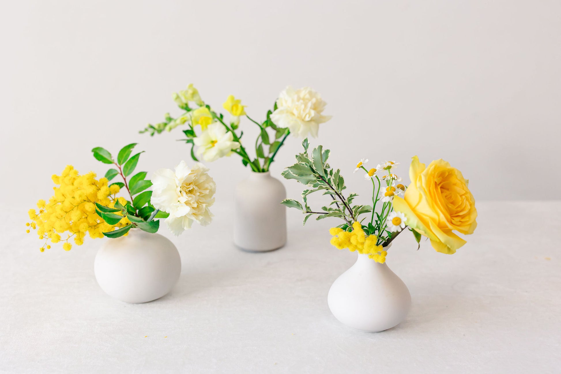 Yellow flowers in white bud vases on a white background