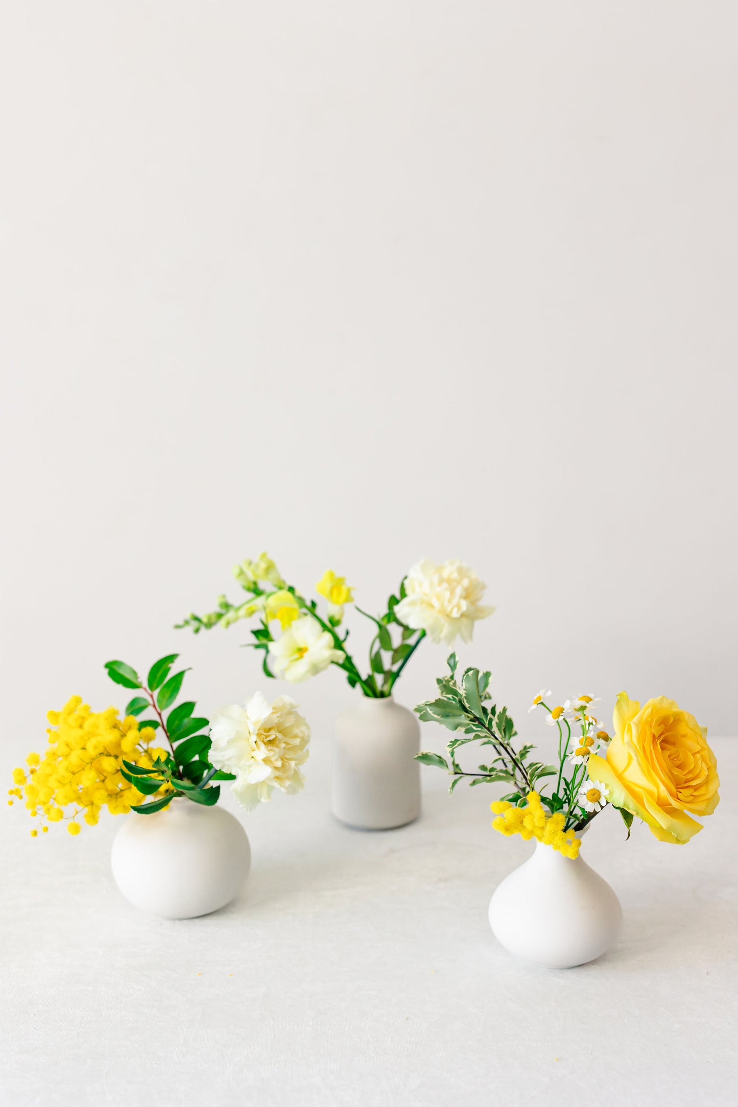 Yellow flowers in white bud vases on a white background