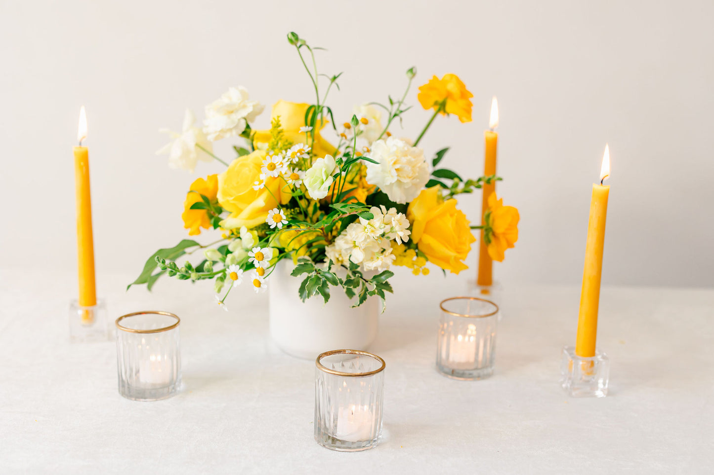 Yellow floral arrangement with yellow candles on a white background