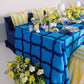 Blue tablecloth with white vases and plates with yellow flower arrangements