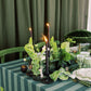 Decorative table setting with candles, plants, and striped tablecloth against a green curtain.