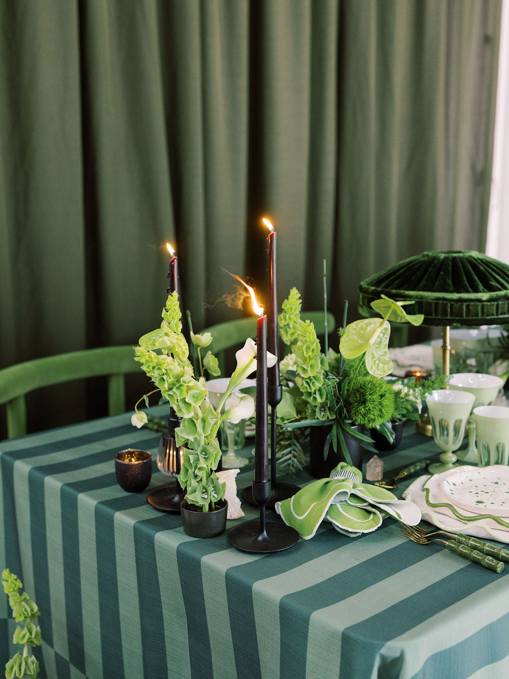 Decorative table setting with candles, plants, and striped tablecloth against a green curtain.