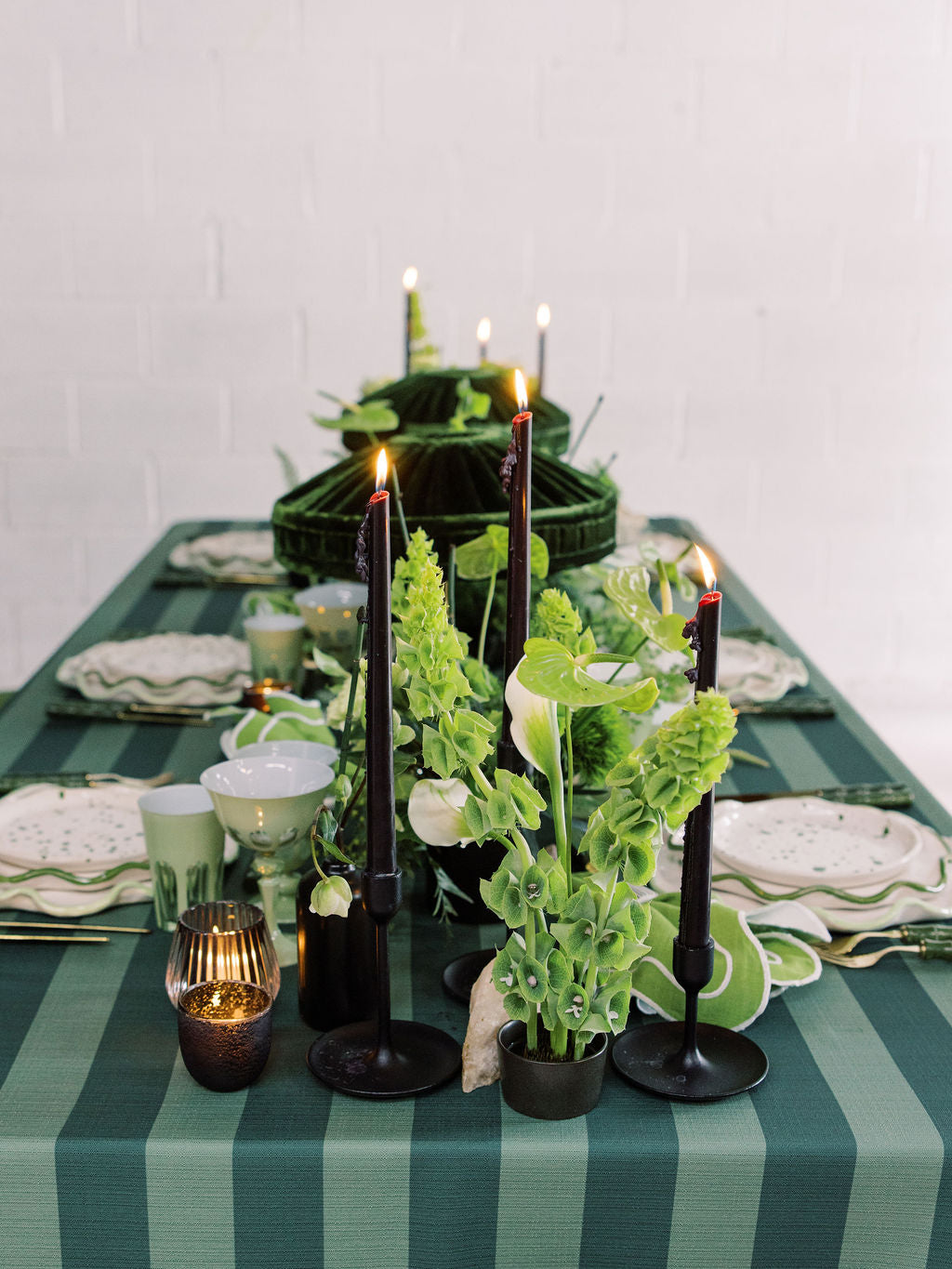 Decorative table setting with candles, plants, and striped tablecloth.