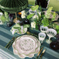 Elegant table setting with green and white decor, including plates, cutlery, and floral arrangements.