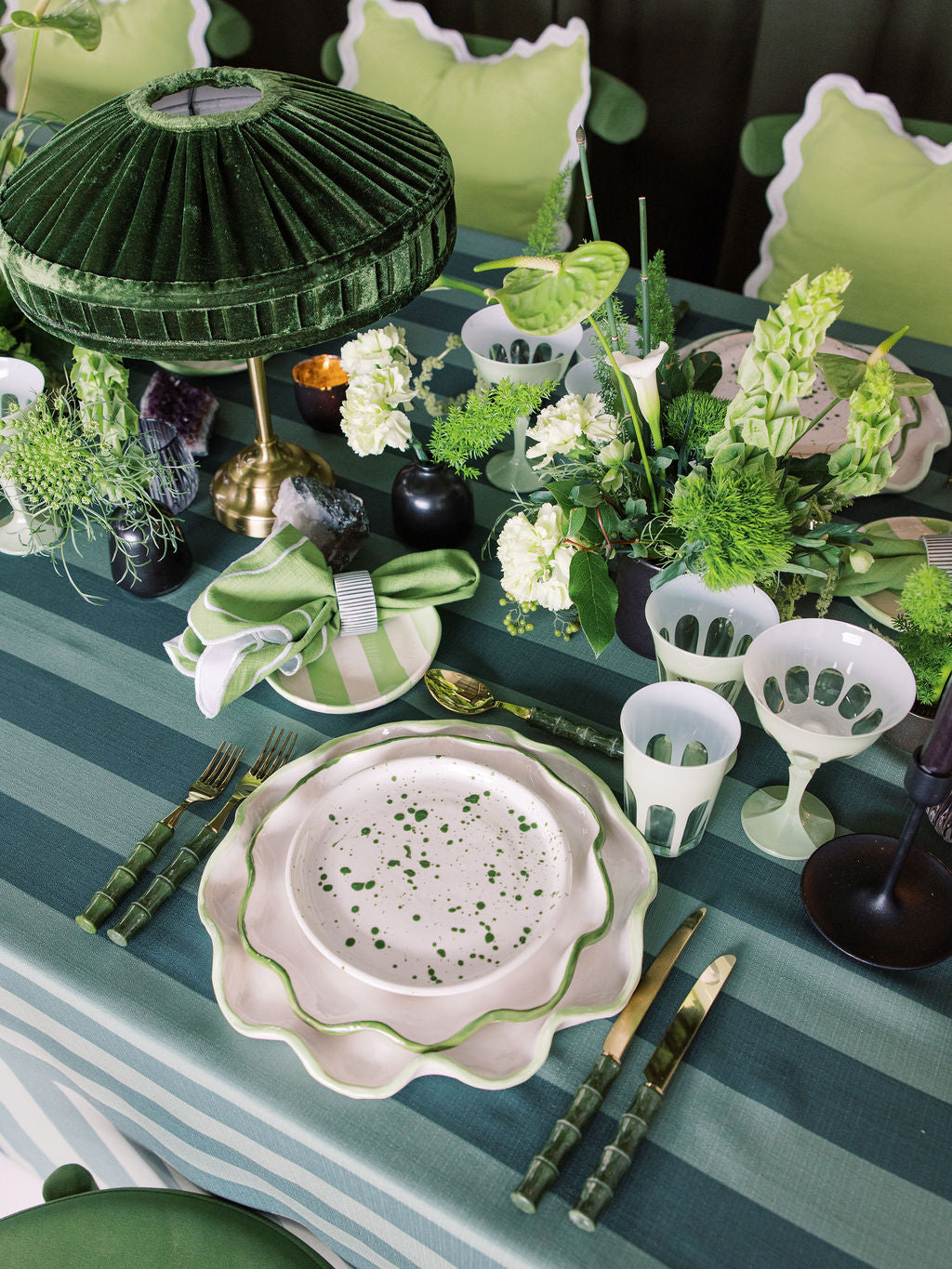 Elegant table setting with green and white decor, including plates, cutlery, and floral arrangements.