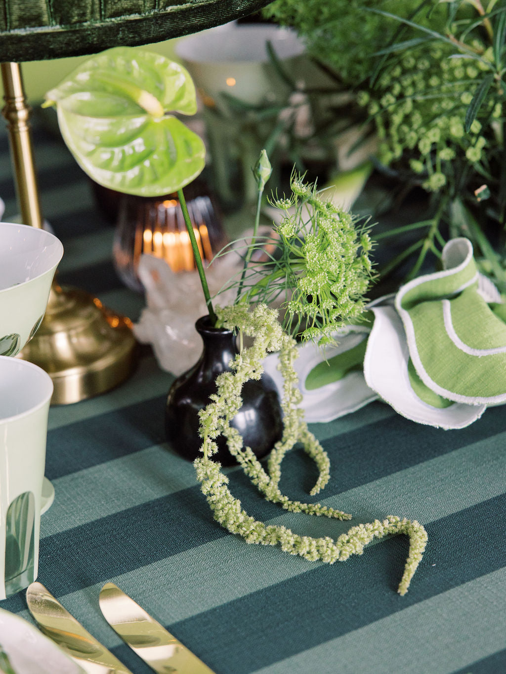 Decorative table setting with greenery, vases, and striped tablecloth.