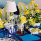 Decorative table setting with yellow and white flowers, blue glasses, and a blue tablecloth.