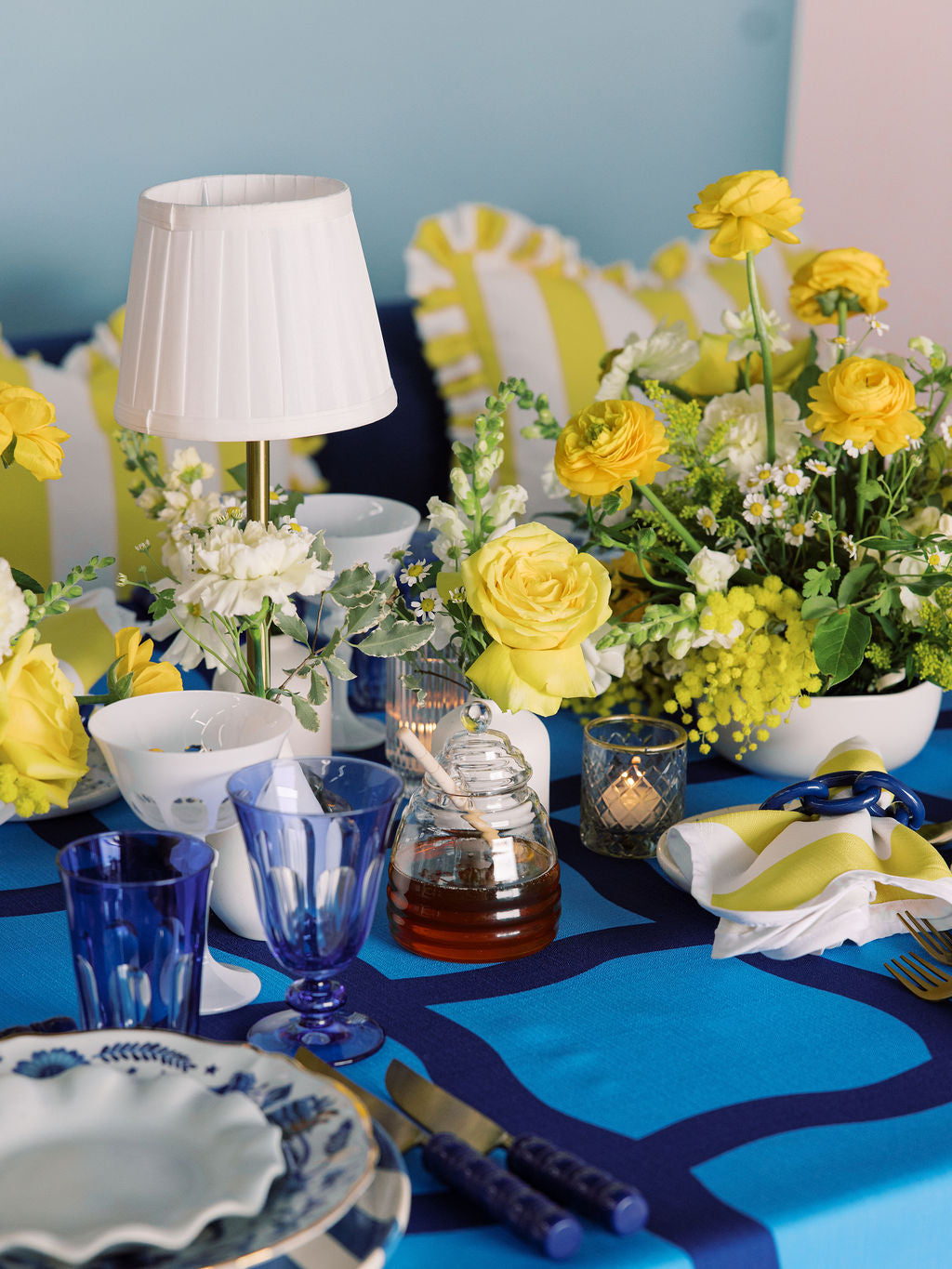 Decorative table setting with yellow and white flowers, blue glasses, and a blue tablecloth.