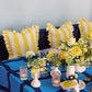 Blue table with white vases and yellow flowers with yellow striped pillows in the background