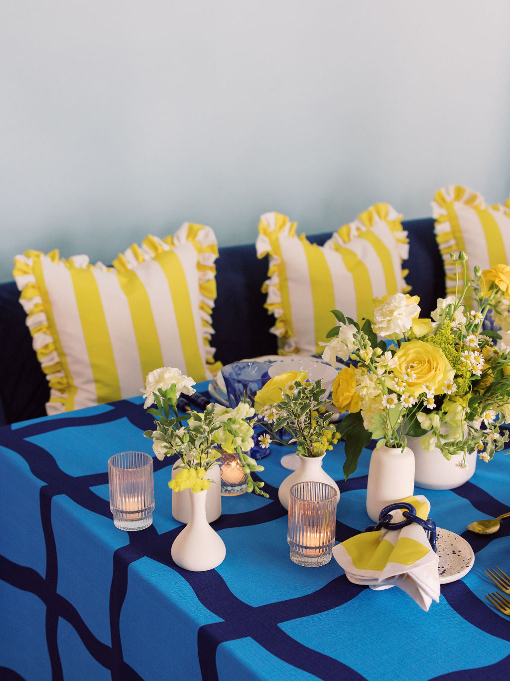Blue table with white vases and yellow flowers with yellow striped pillows in the background
