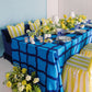 Dining table set with blue and white checkered tablecloth, yellow striped chairs, and floral decorations.