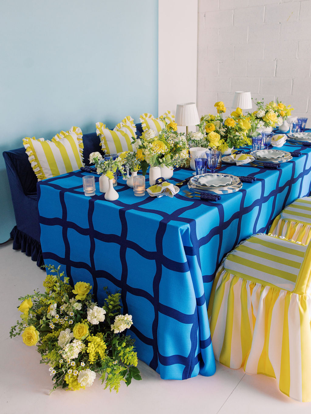 Dining table set with blue and white checkered tablecloth, yellow striped chairs, and floral decorations.