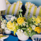 yellow floral arrangement on a blue table with white and yellow striped pillows in the background