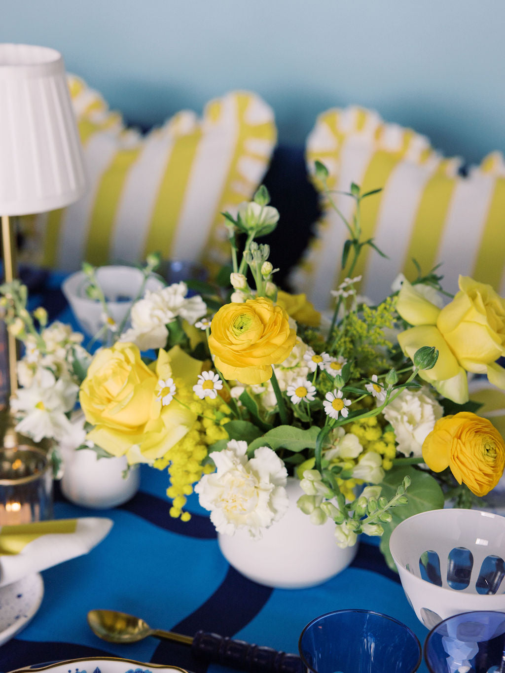 yellow floral arrangement on a blue table with white and yellow striped pillows in the background