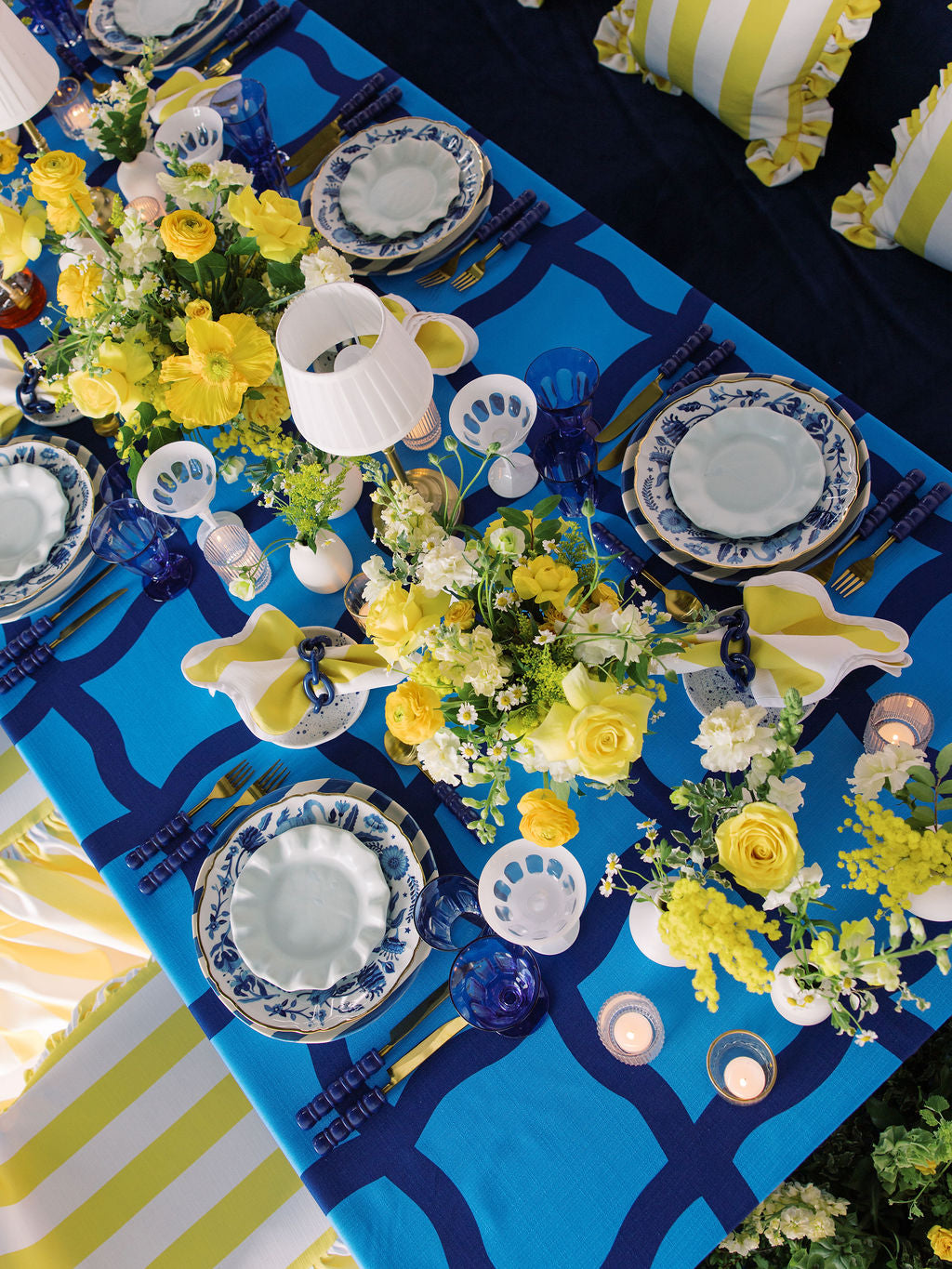 Decorative table setting with blue and yellow tablecloth, floral arrangements, and white plates.