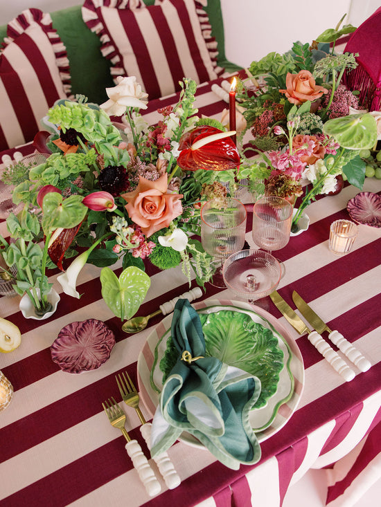 Decorative table setting with floral arrangements, candles, and cutlery on a striped tablecloth.