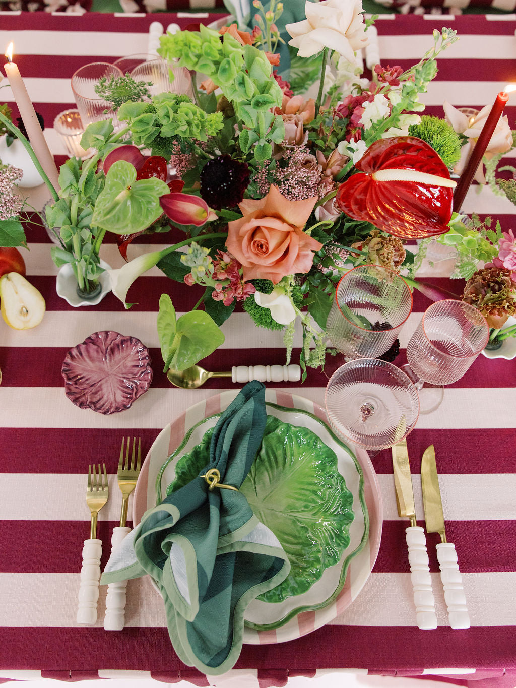 Decorative table setting with floral arrangements, plates, and cutlery on a striped tablecloth.