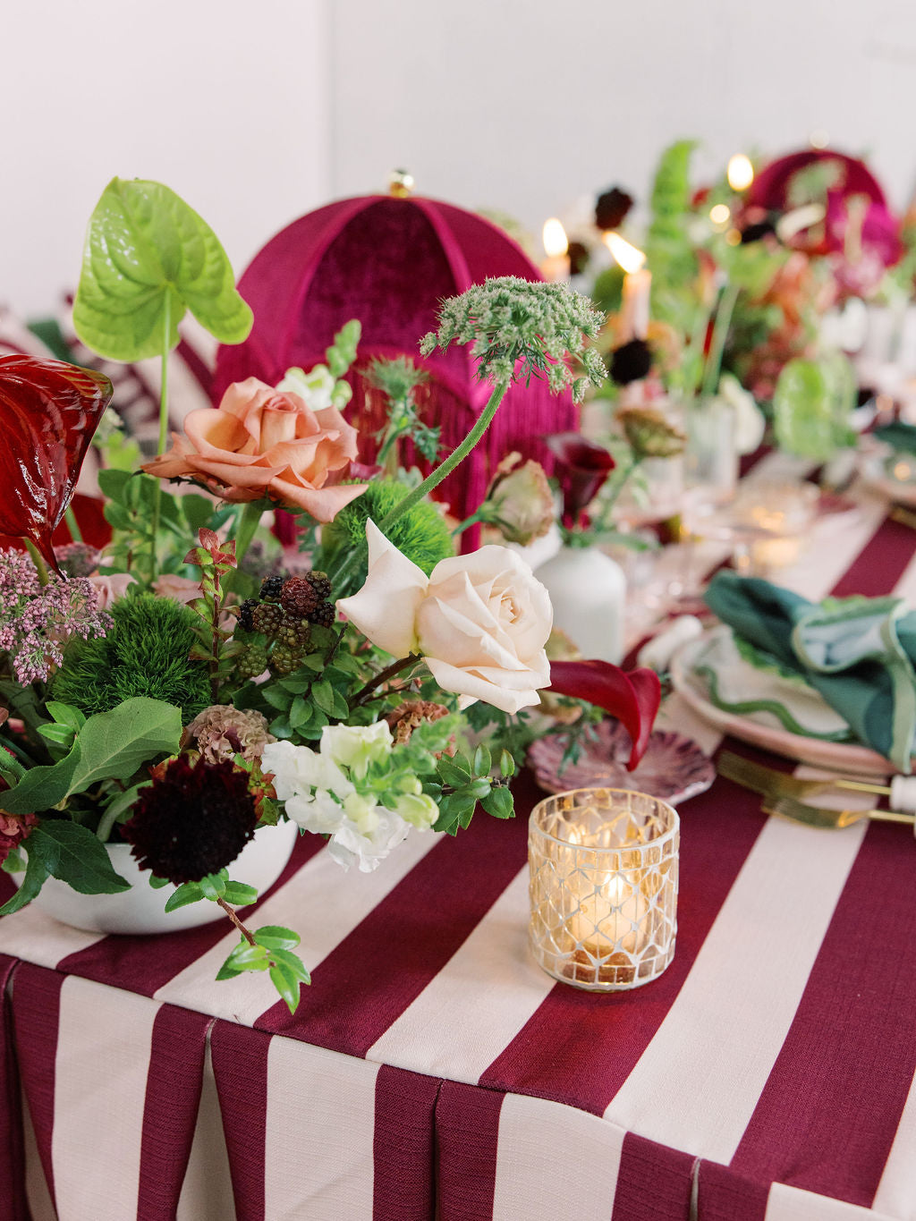 Decorative table setting with flowers, candles, and striped tablecloth.