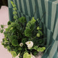 Green floral arrangement with white flowers on a striped tablecloth.