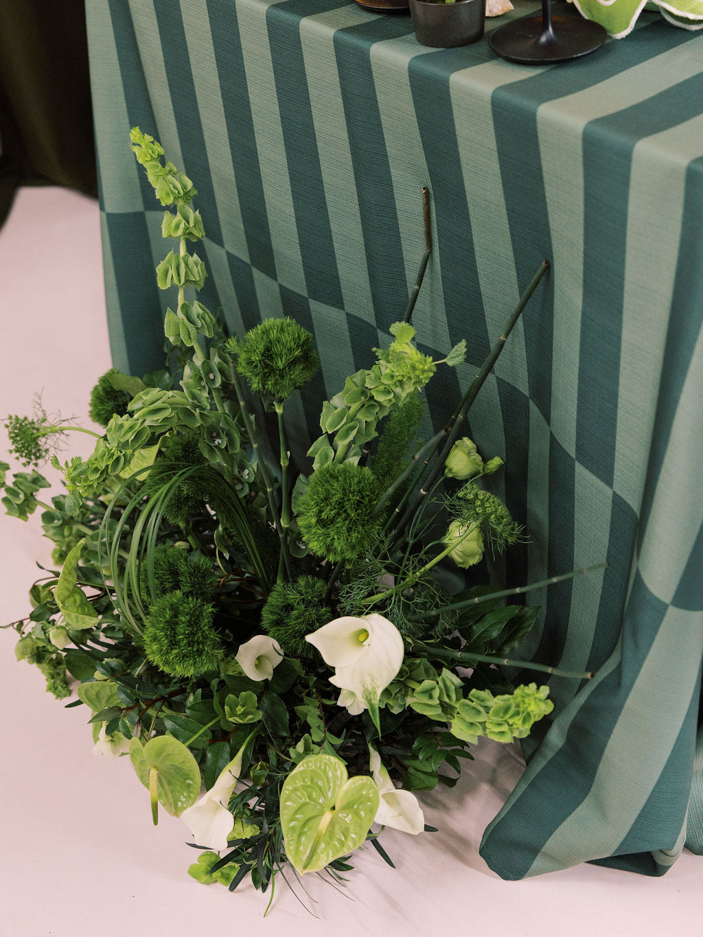 Green floral arrangement with white flowers on a striped tablecloth.