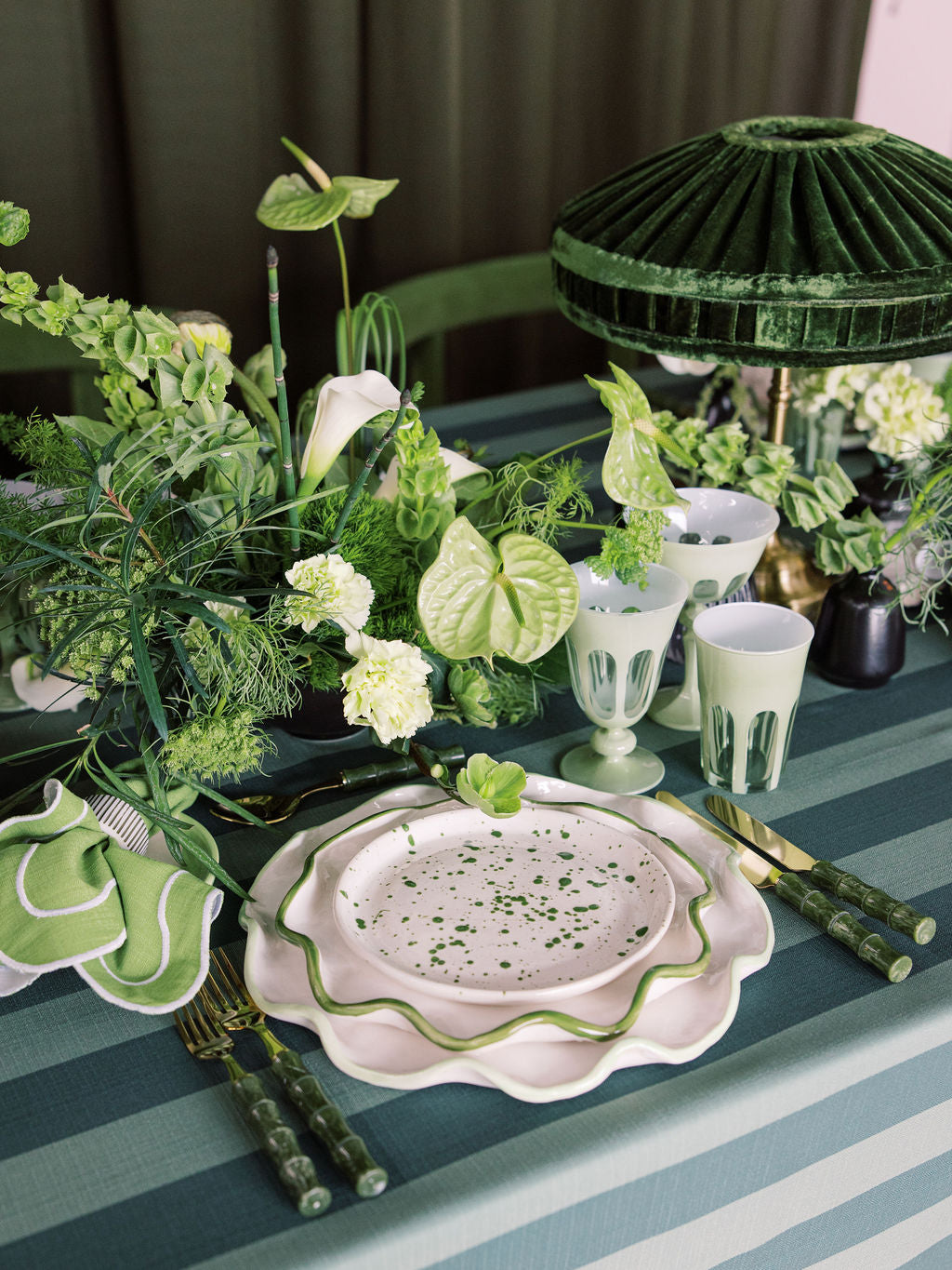 Elegant table setting with green and white decor, including plates, napkins, and a lamp.