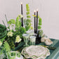 Decorative table setting with green and white elements, including candles and plants, on a striped tablecloth.