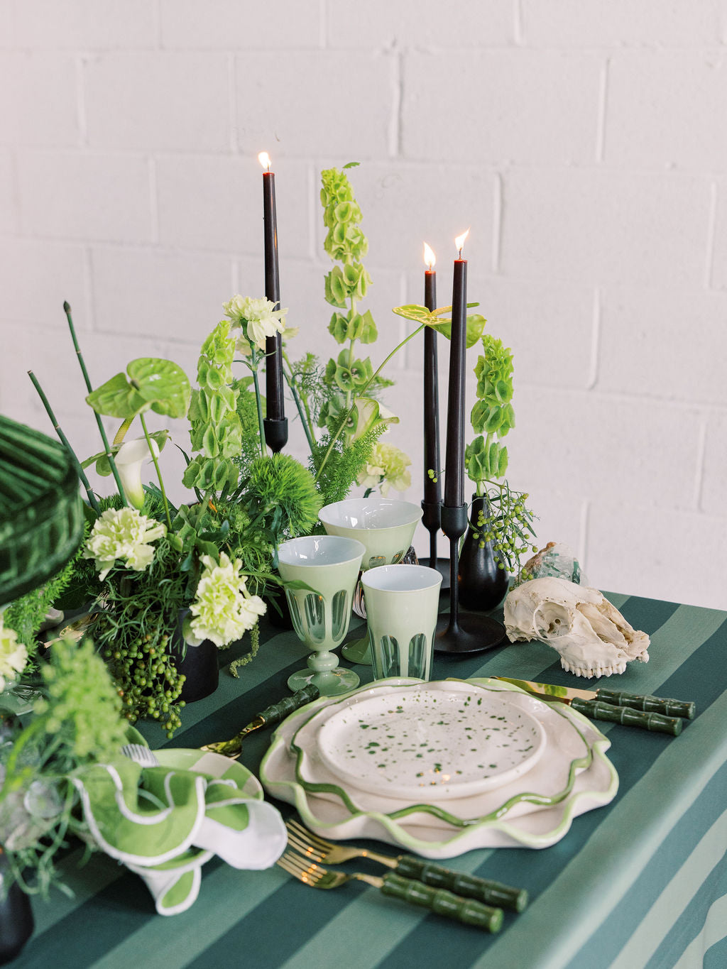 Decorative table setting with green and white elements, including candles and plants, on a striped tablecloth.