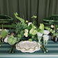 Decorative table setting with green and white elements, including plants and tableware.