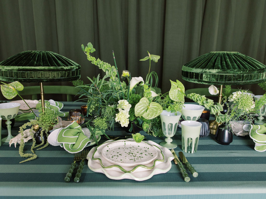 Decorative table setting with green and white elements, including plants and tableware.