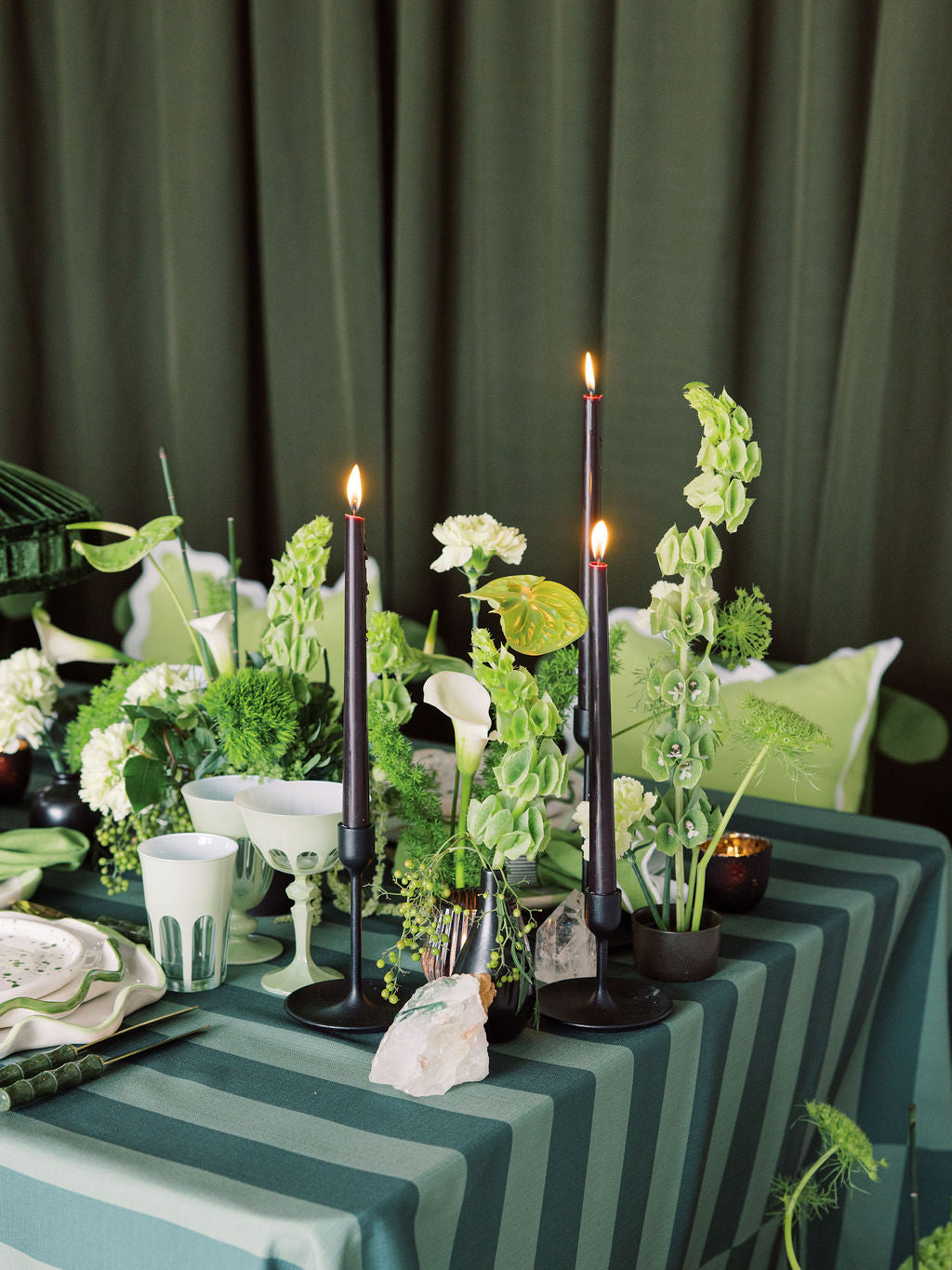 Decorative table setting with candles, flowers, and striped tablecloth against a green curtain.